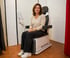 Eine Frau sitzt lächelnd auf einem Pelvipower-Beckenbodentrainer in einem hellen Therapieraum.