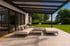 Moderne Terrasse mit hellgrauen Fliesen, beigem Sofa und Couchtisch unter einer schwarzen Pergola.