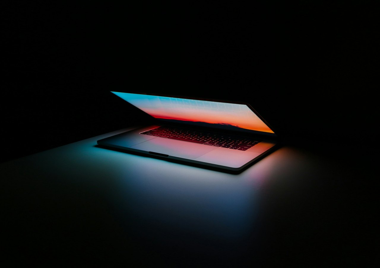 Ein halb aufgeklappter Laptop leuchtet in einem dunklen Raum