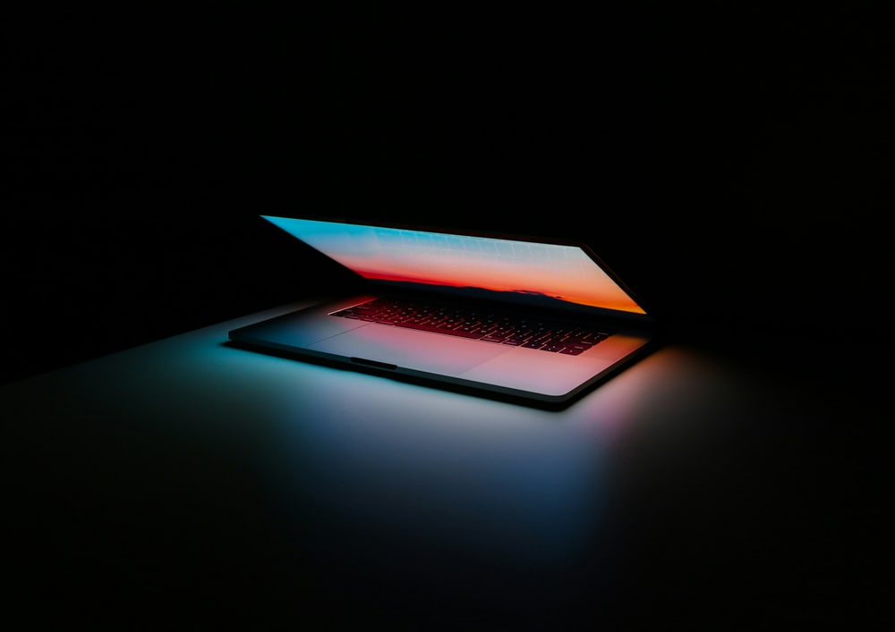 Ein halb aufgeklappter Laptop leuchtet in einem dunklen Raum