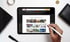 Hand, die einen Stift auf einem Tablet hält, das einen Online-Angebotsrechner mit Produktbildern anzeigt.