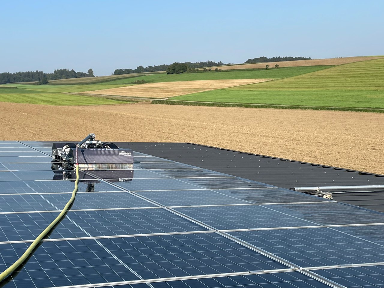 Reinigungsroboter fährt über eine Photovoltaik-Anlage, die Fahrspur zeigt den Unterschied zwischen gereinigter und verschmutzter Fläche