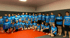 Gruppe von etwa 30 Erwachsenen und Kindern in blauen T-Shirts mit dem Text "AFIGHT" auf rotem Mattenboden.