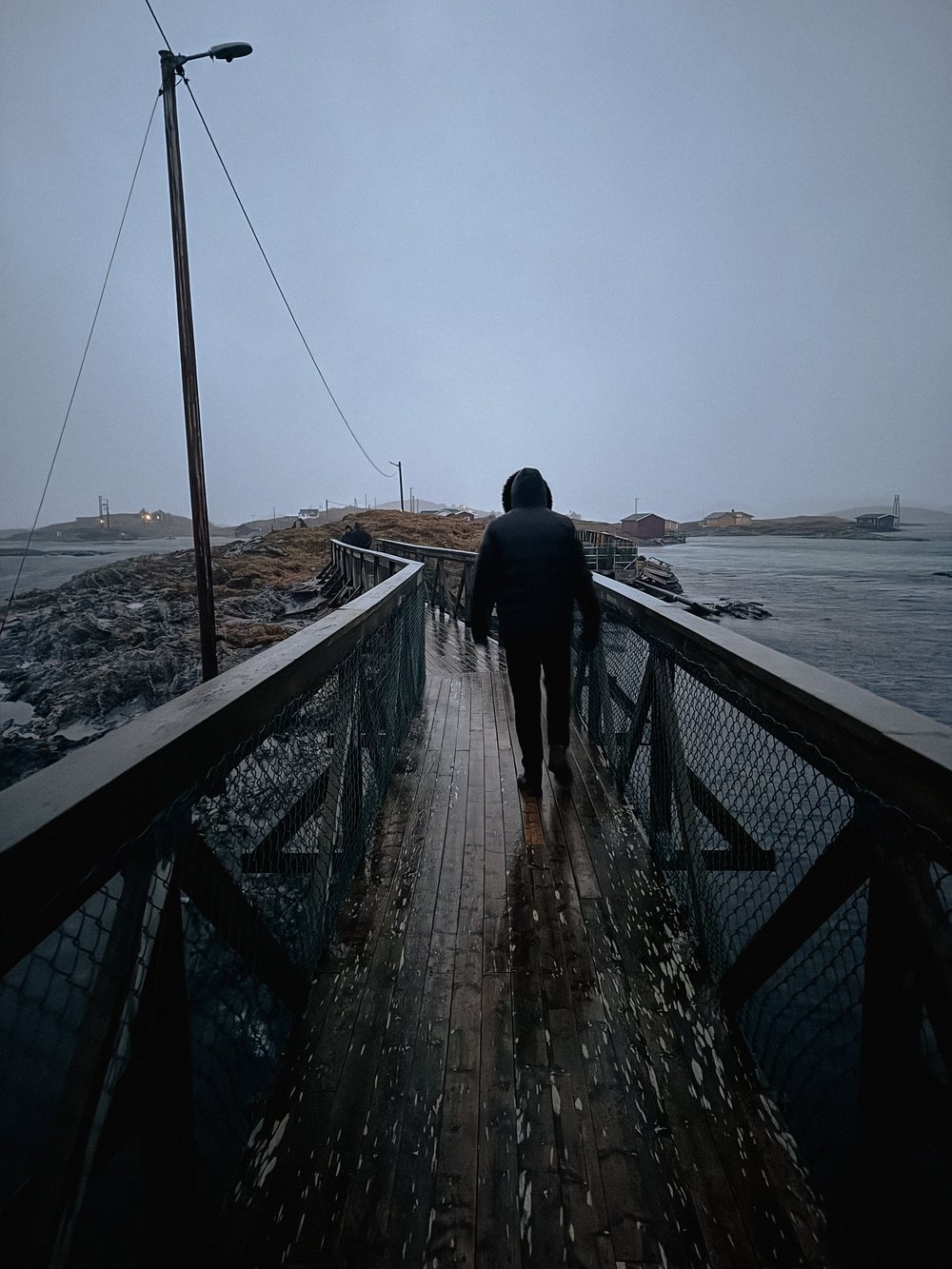 Person geht über eine Holzbrücke am Meer