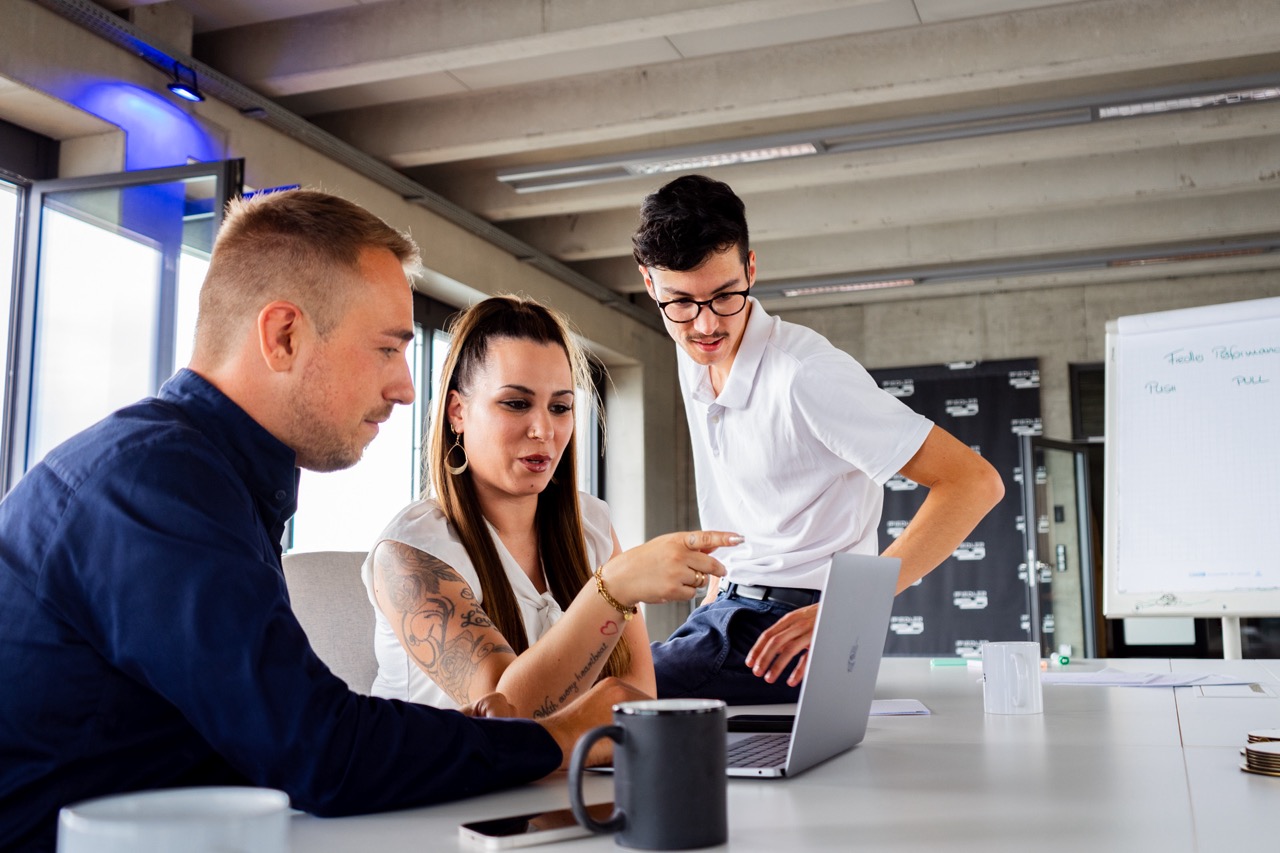 Drei Personen besprechen gemeinsam Inhalte an einem Laptop im Büro