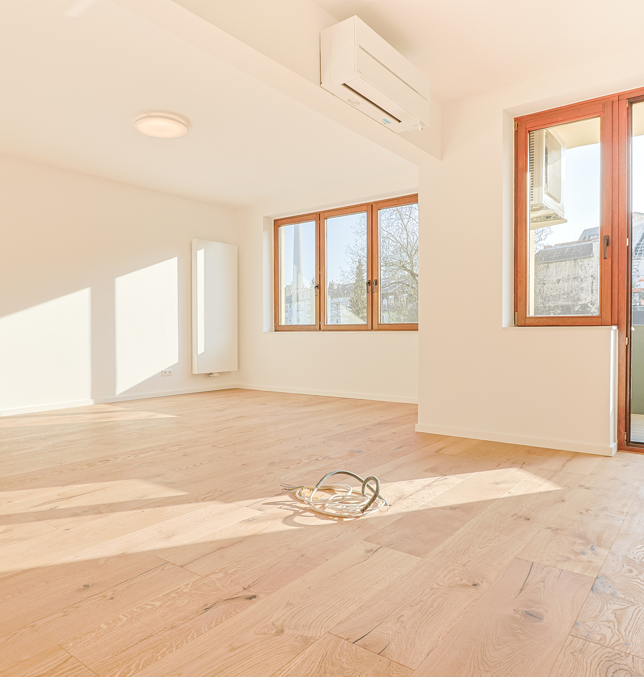 Modern saniertes Wohnzimmer mit Echtholzparkett, weißen Wänden, großen Fenstern und Klimaanlage