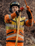 Feuerwehrmann in orangefarbener Jacke und Helm bindet ein Seil mit einem Karabiner.