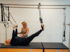 Eine Frau trainiert an einem Pilates-Cadillac-Gerät unter Anleitung einer Trainerin in einem hellen Studio.
