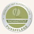 Graues Qualitätssiegel mit der Aufschrift „QUALITÄT MIT AUSZEICHNUNG FACHINSTITUT FUSSPFLEGE“ und einem Logo.