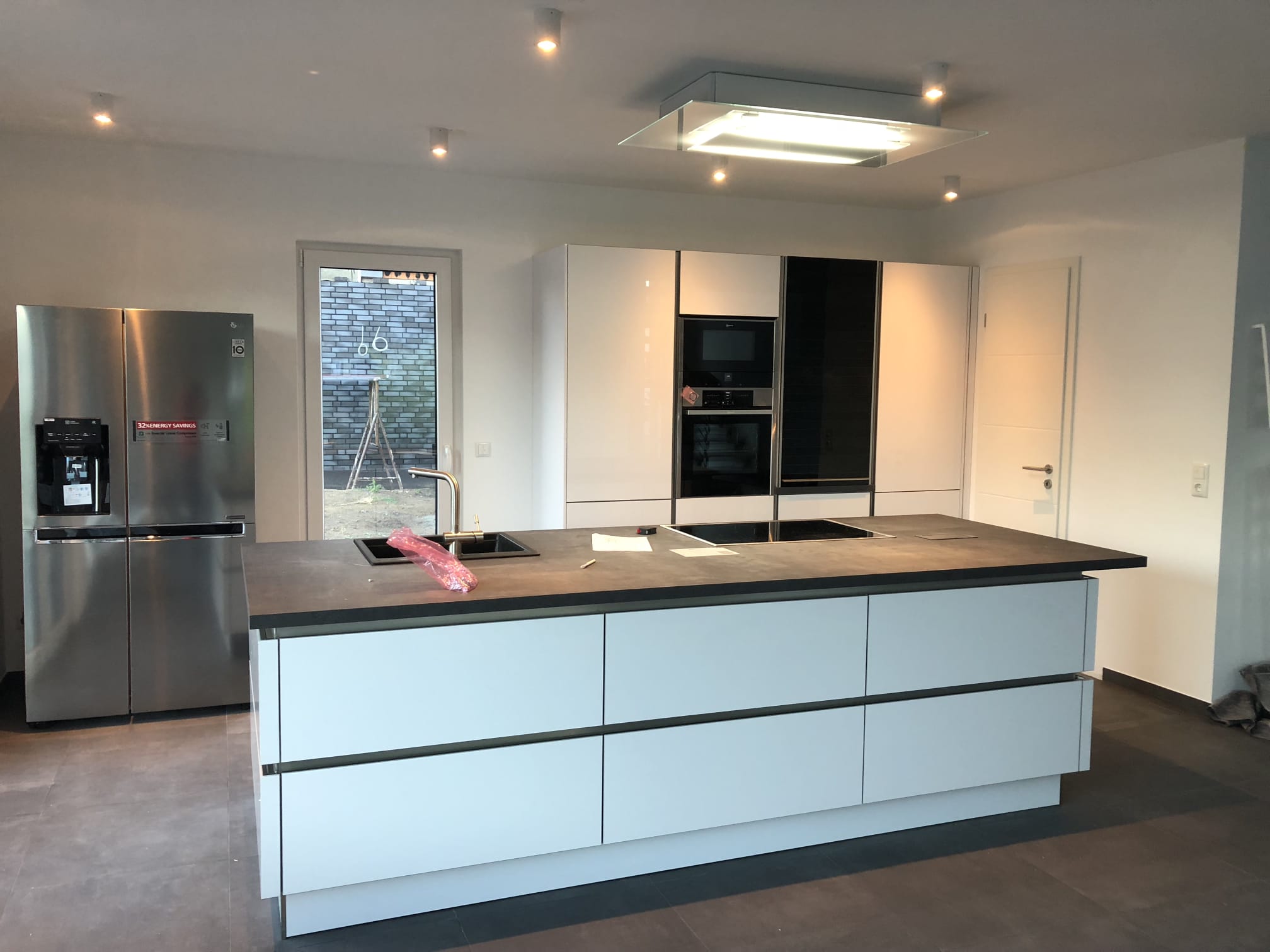 Weiße Kücheninsel mit grifflosen Fronten, Gerätehochschränken und Side-by-Side-Kühlschrank