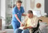 Nurse assisting an elderly man with Parkinson’s as he writes in a notebook.