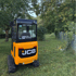 Ein gelber JCB-Minibagger steht auf einer grünen Grasfläche neben einem Baum und einem Zaun.