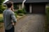 Ein nachdenklicher Mann betrachtet die gepflasterte Hauseinfahrt und Garage eines Einfamilienhauses.