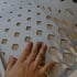 Eine Hand berührt eine perforierte Metallplatte mit blattförmigen Ausschnitten.