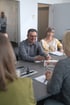 Ein lächelnder Mann demonstriert einer Gruppe an einem Tisch ein medizinisches Gerät zur Pulsoximetrie.