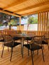 Holzterrasse mit Esstisch, sechs Stühlen, Glasvase und Blick auf Meer und Bäume.