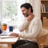 A man sitting at a desk with a laptop grimaces while holding his hand to the side of his neck.