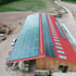 Rotes Scheunendach mit großen Solarpanelen auf beiden Seiten, umgeben von Schotter und grünen Feldern.