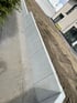 Eine Stützmauer aus L-Steinen aus Beton trennt einen gepflasterten Weg von einer Erdaufschüttung vor einem Wohnhaus.