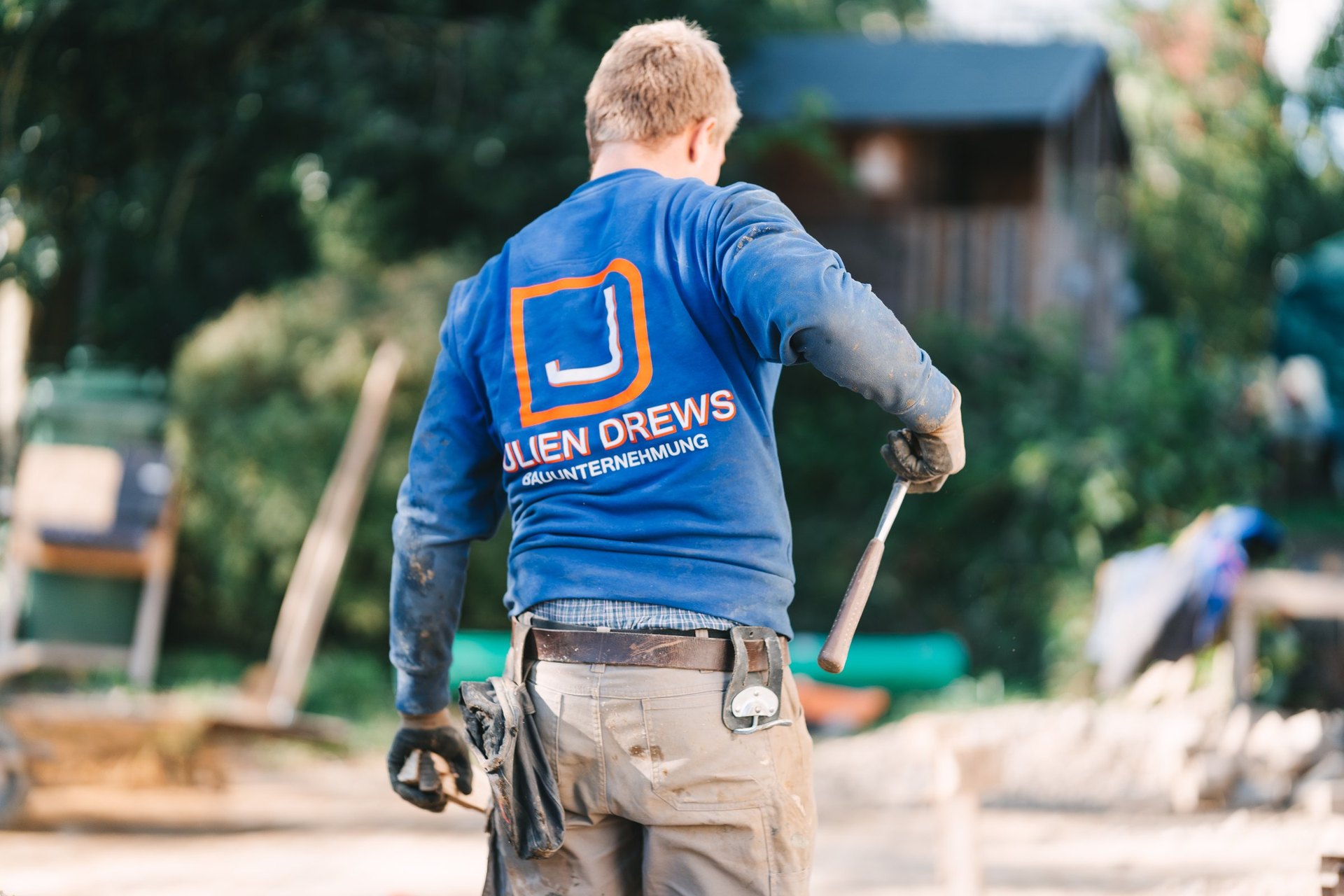 Julien Drews bei der Arbeit auf einer Baustelle, von hinten mit Firmenlogo auf dem Pullover