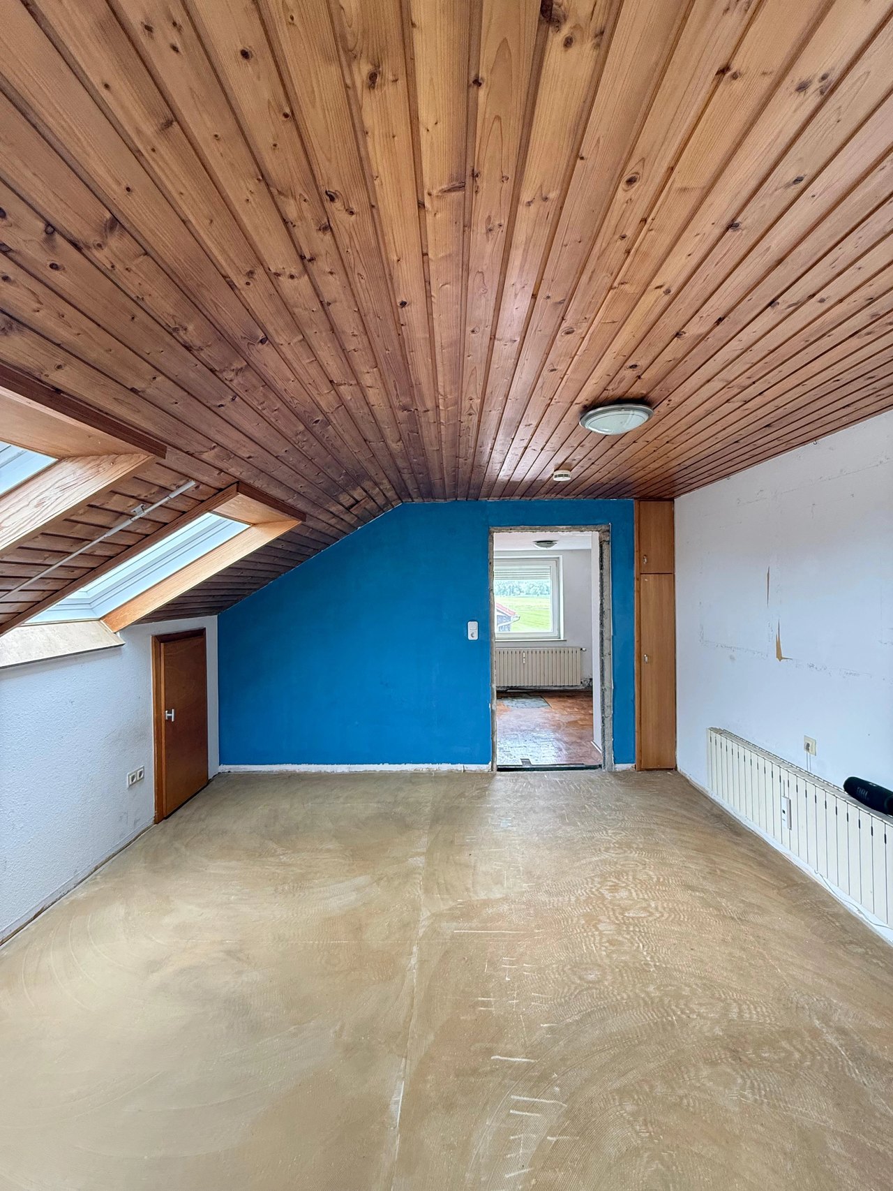 Leergeräumtes Dachgeschosszimmer mit Holzdecke und blauer Wand nach einer Räumung in Füssen