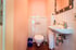 Kleines Badezimmer mit rosa Wänden, weißer Toilette, Waschbecken, Seifenspender und Spiegel.