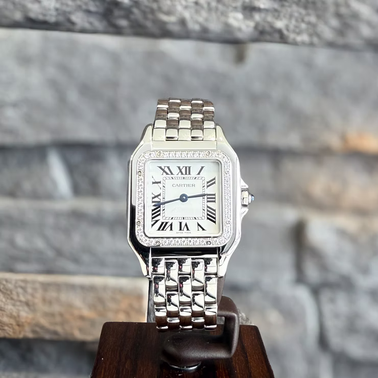 Cartier Panthère Stahl Damenuhr mit Diamanten auf einem Holzständer vor einer grauen Steinwand.