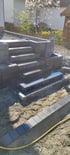 Neu gebaute Außentreppe aus grauen Betonblockstufen auf einer Gartenbaustelle mit Sand und Einfassungssteinen.
