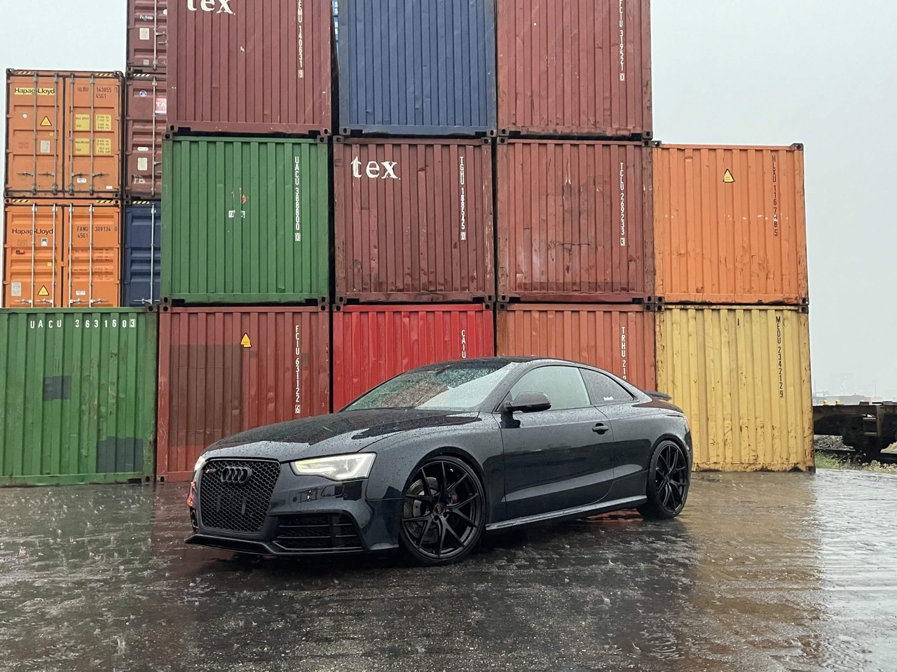 Black Audi coupe with TEC Speedwheels GT 6 EVO wheels in front of containers
