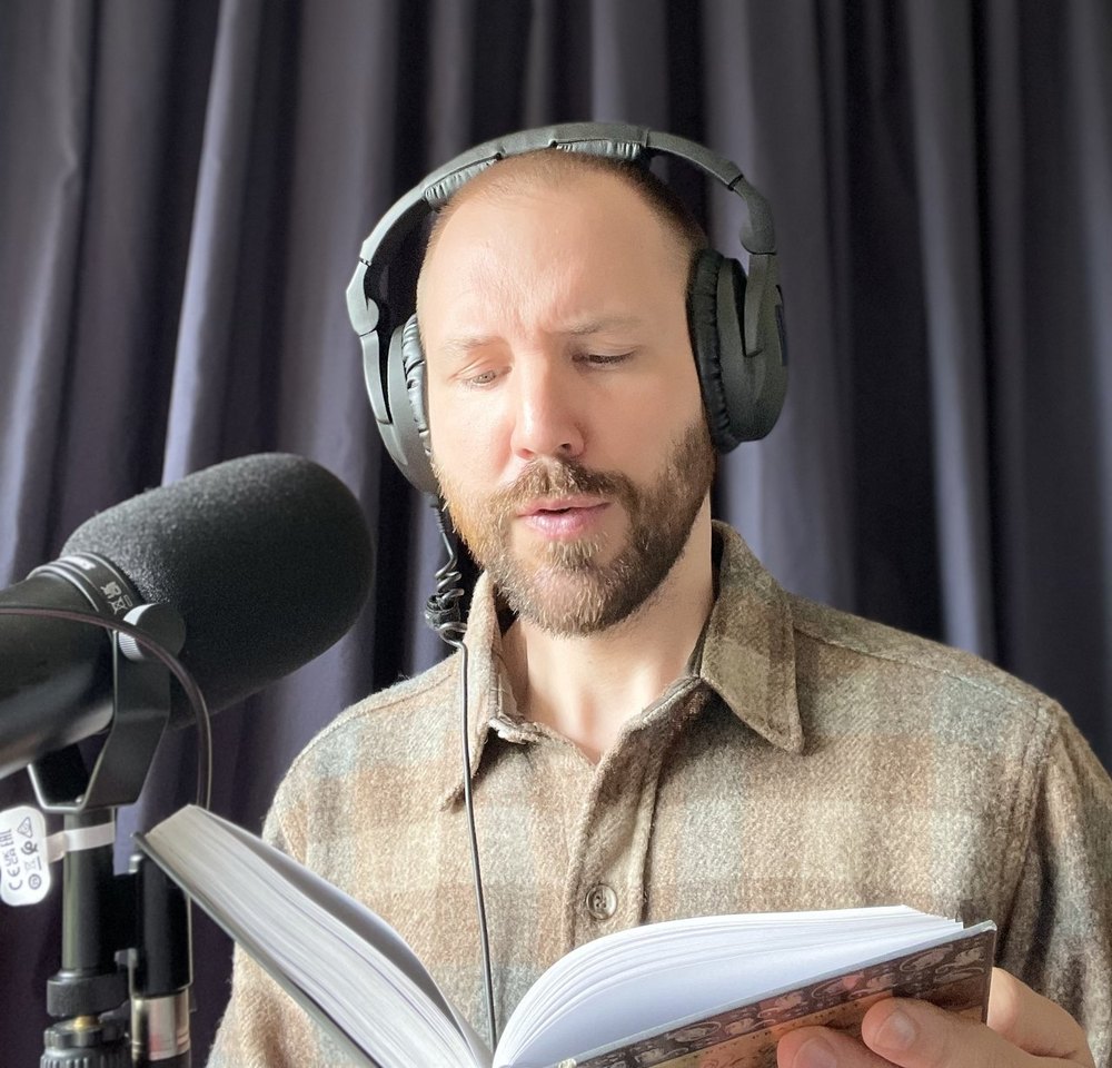 Pierre Huber liest ein Buch am Mikrofon ein, Hörbuchproduktion im Studio