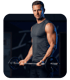 Muskulöser Mann im ärmellosen Shirt, der eine Langhantel im Fitnessstudio hält und direkt in die Kamera blickt.