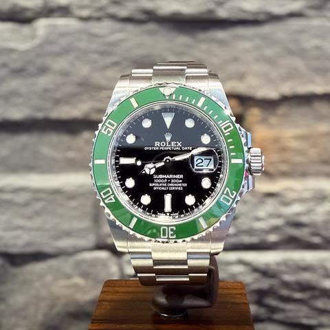 Silberne Rolex Submariner Uhr mit schwarzem Zifferblatt, grüner Lünette und Datumsanzeige auf 27, auf Holzständer.