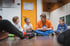 Ein Erwachsener sitzt mit drei Kindern im Kreis auf dem Boden und unterhält sich, im Hintergrund eine orangefarbene Tür.