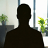 Silhouette eines Mannes vor einem Fenster, Pflanzen und Büromöbel im Hintergrund.
