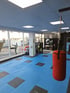 Fitnessraum mit blauen und schwarzen Matten, einem roten Boxsack und einer Silhouette eines Kickboxers an der Fensterscheibe.