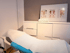 Behandlungsliege in einer Praxis mit weißer Kommode, Handtuch und anatomischen Postern zu Reflexzonen an der Wand.