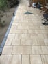 Neu verlegter Gartenweg aus hellbeigen Pflastersteinen mit dunkler Randsteinfassung und Gartenwerkzeugen im Hintergrund.