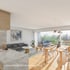 Modernes Wohnzimmer mit offenem Essbereich, Holztisch, grauem Sofa und Balkon mit Blick ins Grüne.