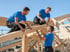Drei Zimmermänner in blauen T-Shirts montieren ein Holzdach auf einer Baustelle.