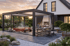 Moderne Pergola mit Glaswänden, Jacuzzi und einer Außenküche vor einem Haus bei Sonnenuntergang.