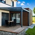 Moderne Terrasse mit Holzdeck, anthrazitfarbener Pergola und Gabionenbank vor einem Haus.