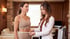 A female doctor in a white coat uses a measuring tape to measure the waist of a woman in tan athletic wear.