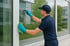 Mann in blauer Uniform und Handschuhen putzt ein Fenster mit einem Abzieher und einem grünen Tuch.