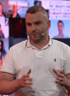 Ein Mann mit kurzem Haar und weißem Poloshirt spricht ins Mikrofon, gestikuliert mit den Händen.
