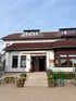 Eingangsbereich der Gartenkantine Rothenburgblick mit Steintreppe, Blumenkästen und weißer Fassade unter blauem Himmel.