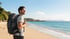 Lächelnder Mann mit Rucksack am Strand, blickt auf das Meer und die Küste.