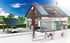 Haus mit Solarpaneelen auf dem Dach, angeschlossen an ein Elektroauto, das unter einem Solar-Carport geparkt ist.