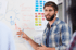 Mann im karierten Hemd präsentiert Ideen auf einem Whiteboard mit "Themes", "Seaside Towns", "City", "Country" und Farbpalette.