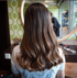 Rückenansicht einer Frau mit langen, glänzenden, braunen Haaren mit helleren Balayage-Wellen.