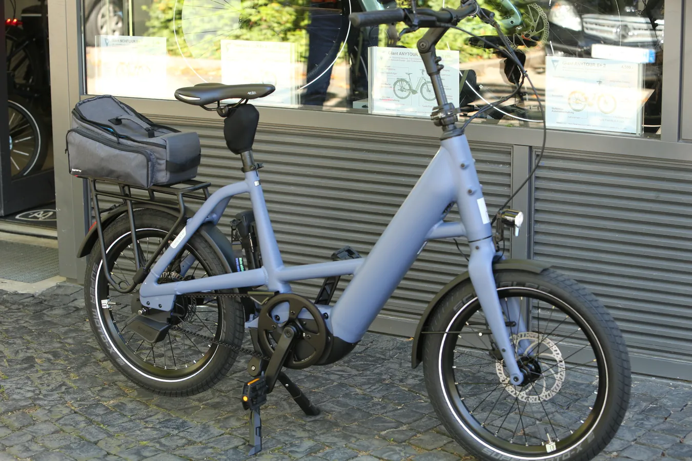 Blaues Kompakt-eBike mit Gepäcktasche vor dem Laden